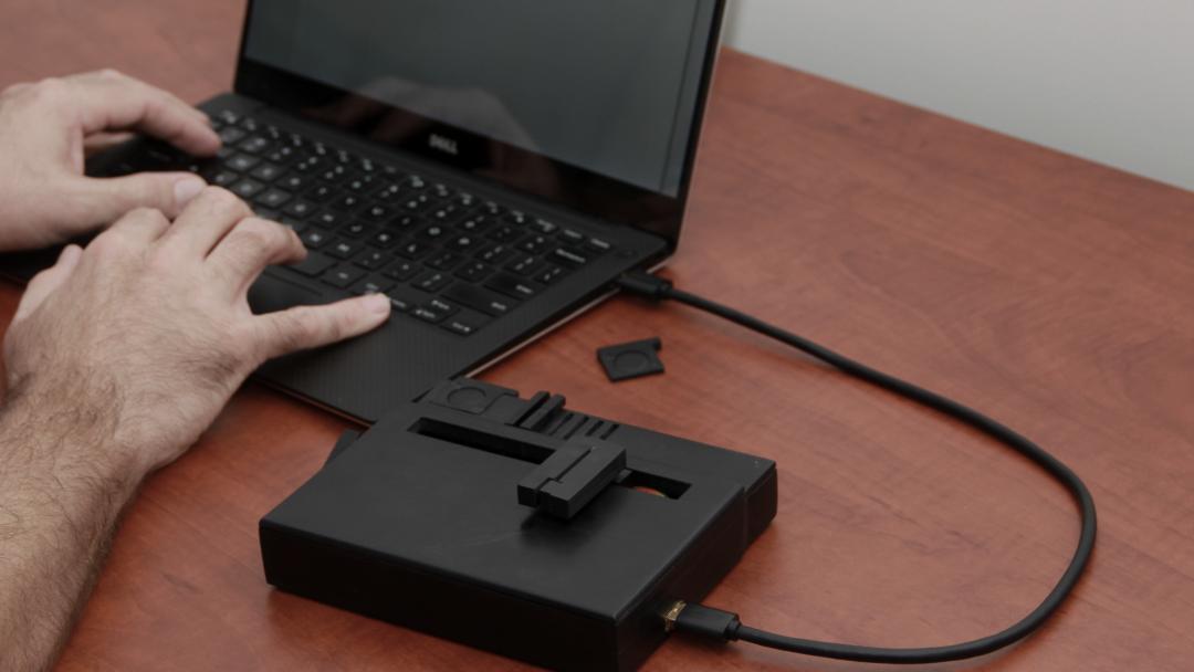 The KInD system in use on a desk. KInD is positioned to the right of a laptop and connected via USB cable.