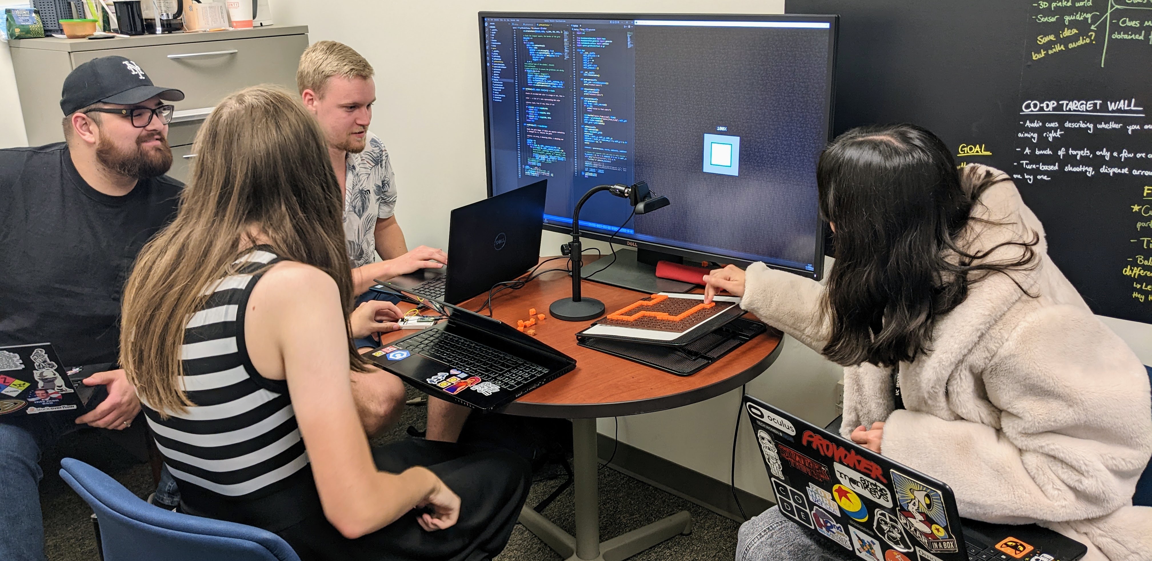 Four students sitting at a table working in front of a large monitor